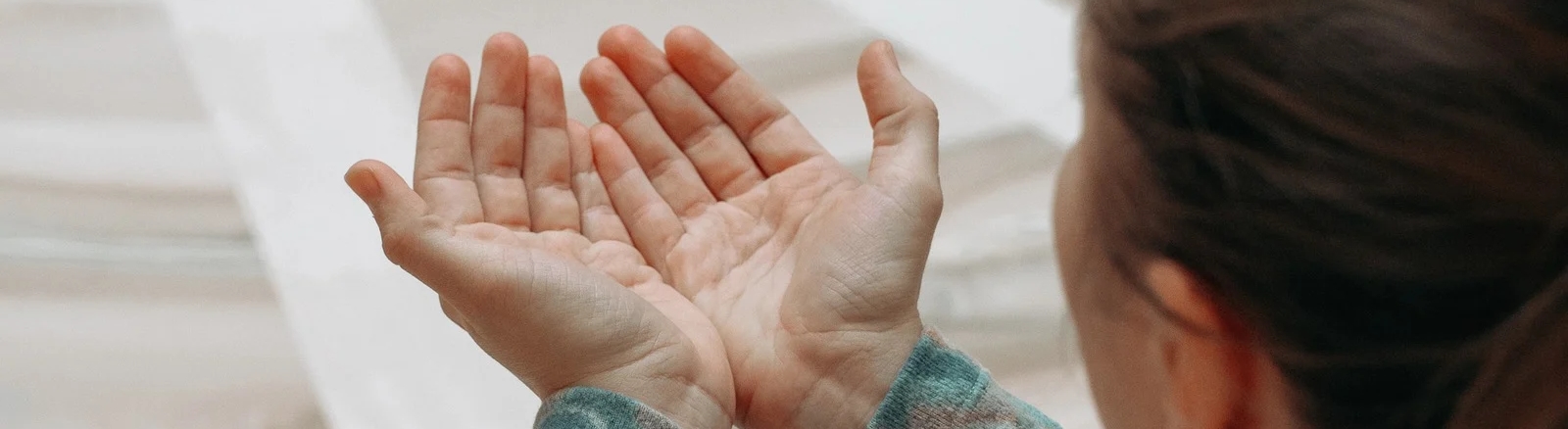 Zwei Frauen liegen entspannt auf sandigem Boden, umgeben von trockenem Schilf. Sie tragen warme, gestrickte Kleidung und strecken ihre Hände in die Luft, während sie die Augen geschlossen halten. Die Szene wirkt ruhig und harmonisch.