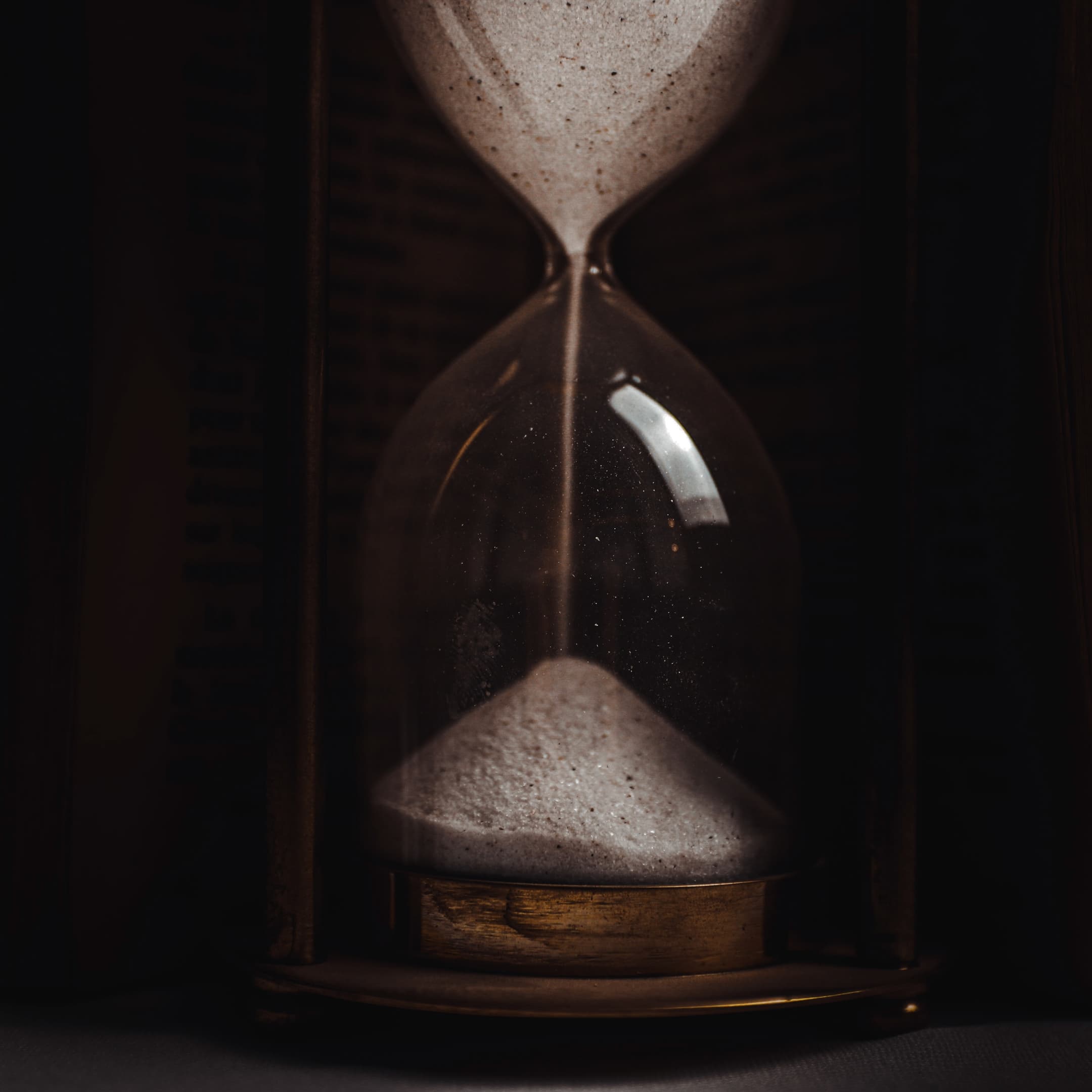 Nahaufnahme einer Sanduhr mit feinem Sand, der von der oberen in die untere Hälfte rieselt. Das Licht betont die Struktur des Glases und den Sand.