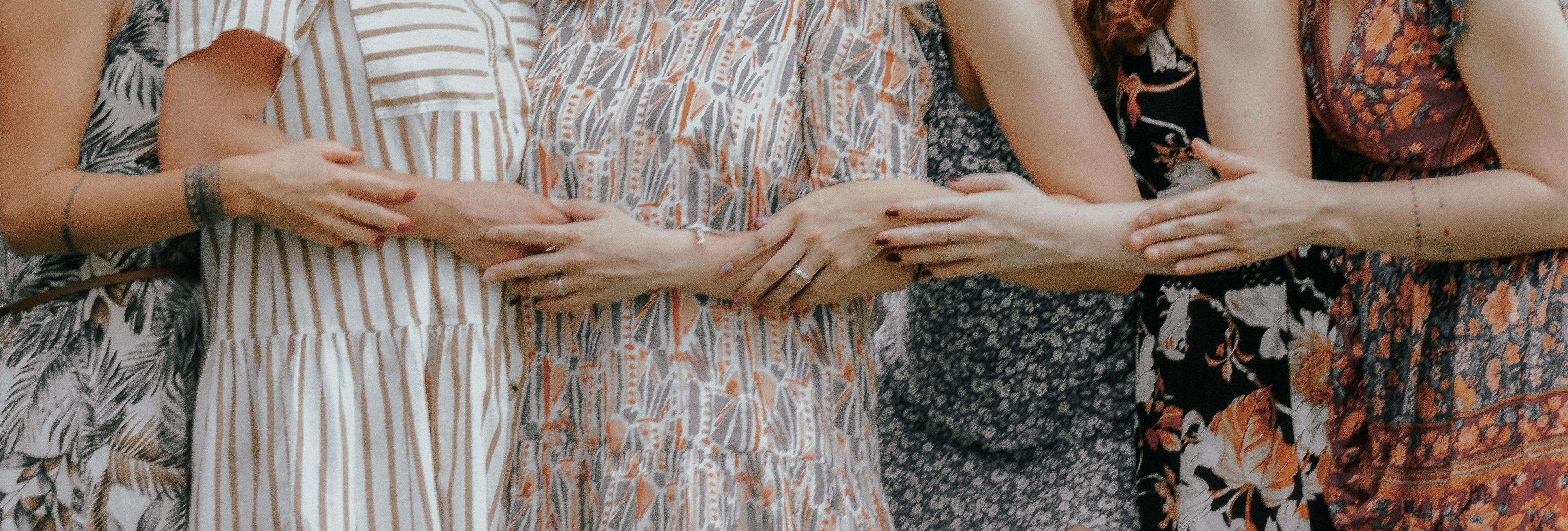 Zwei Frauen strecken ihre Hände sanft in Richtung hängender Zweige einer Weide. Die Szene wirkt ruhig und harmonisch, mit weichen, neutralen Farben.